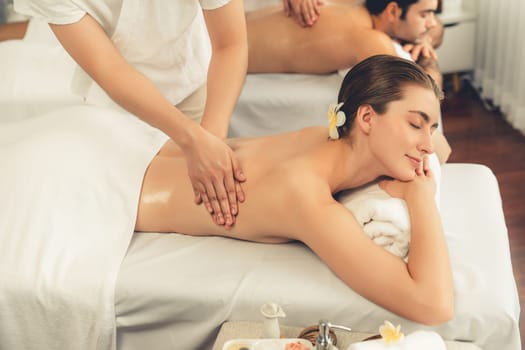 Caucasian couple customer enjoying relaxing anti-stress spa massage and pampering with beauty skin recreation leisure in day light ambient salon spa at luxury resort or hotel. Quiescent