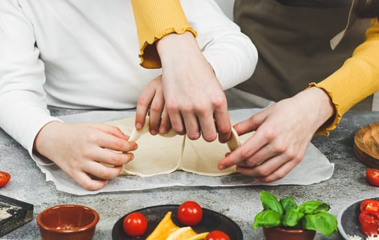 Two pairs of rue Caucasian girls sisters sort out the cut out dough with chopped ingredients on the table, close-up side view. Valentine's day cooking pizza concept.