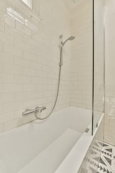 a white bathtub in a bathroom with tiled walls and black and white tiles on the floor, there is a glass shower door