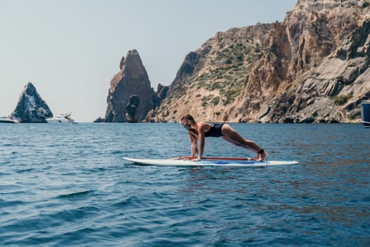 Close up shot of beautiful young caucasian woman with black hair and freckles looking at camera and smiling. Cute woman portrait in a pink bikini posing on a volcanic rock high above the sea