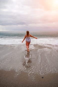 A plump woman in a bathing suit enters the water during the surf. Alone on the beach, Gray sky in the clouds, swimming in winter