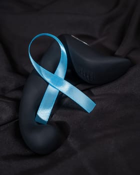 Prostate stimulator and blue ribbon on a black silk sheet. Symbol of the fight against prostate cancer
