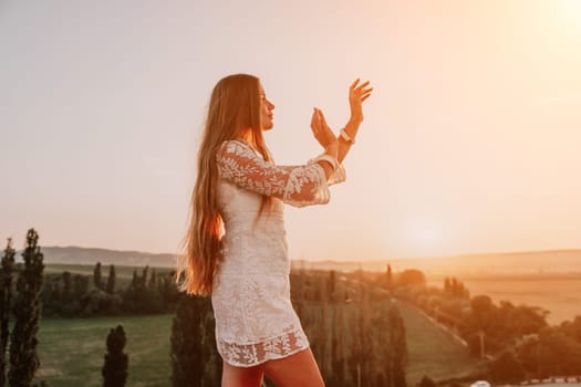 Romantic beautiful bride in white dress posing with sea and mountains in background. Stylish bride standing back on beautiful landscape of sea and mountains on sunset