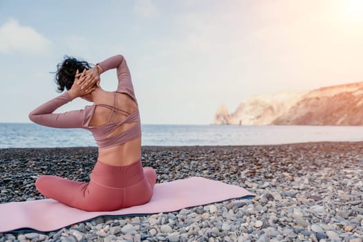 Middle aged well looking woman with black hair doing Pilates with the ring on the yoga mat near the sea on the pebble beach. Female fitness yoga concept. Healthy lifestyle, harmony and meditation.