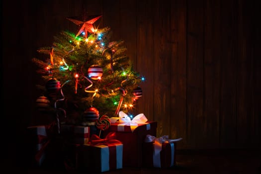 Decorated Christmas tree with glowing lights and gift boxes on wooden background