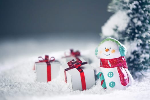 Small cute snowman with gift in fir forest under falling snow
