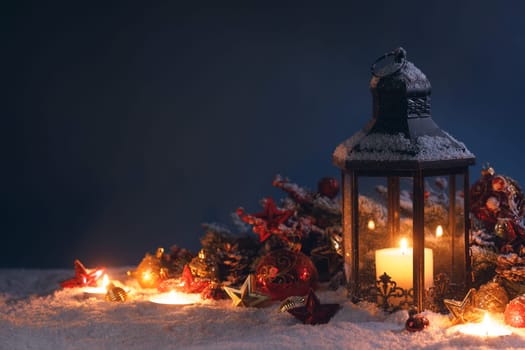 Christmas background with burning candle inside lantern and bauble decorations in snow