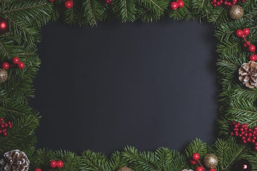 Pine Christmas tree branches and red berries on black paper background flat lay top view mock-up