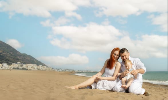 Happy family on vacation sitting on a sand beach with a baby son. Mid shot