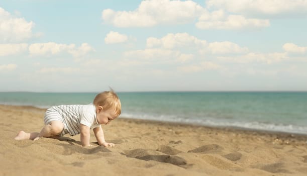 A baby boy crawling on a sand on the seaside. Mid shot