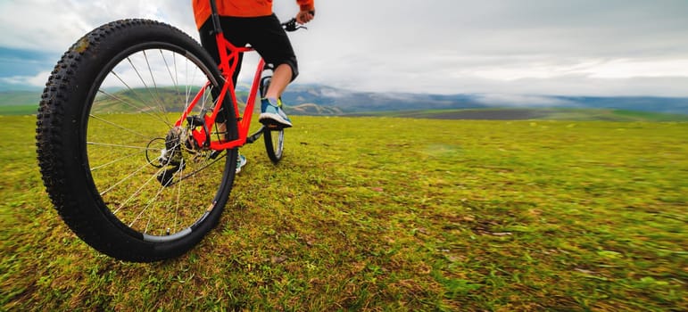 Panoramic shot of a cyclist on a mountain bike against a background of green hills and mountains in the clouds. Mountain bike banner.