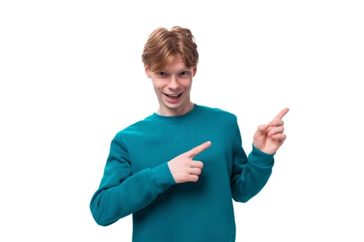 young handsome red-haired man with a blue sweater points his finger at the advertising space.