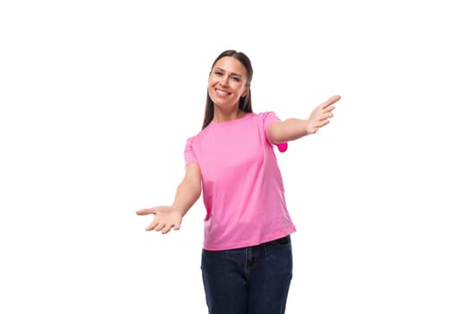 young slim european woman with black straight hair is dressed in a pink t-shirt on a studio background with copy space.