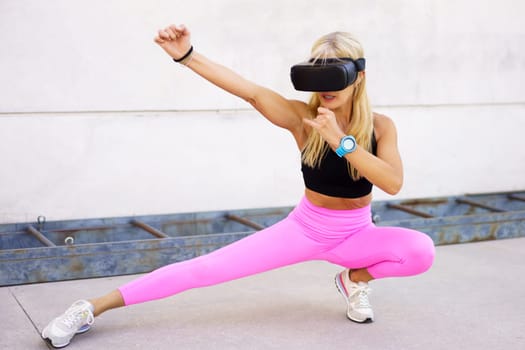 Full body of fit strong female athlete in sportswear and VR headset performing wushu fighting stance while experiencing virtual world