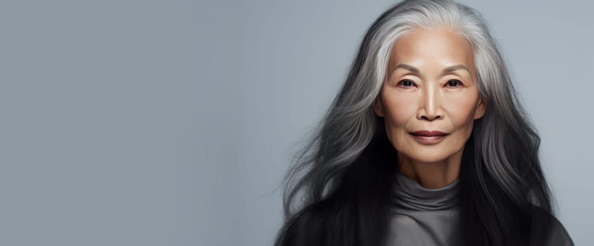 Smiling, elderly, gorgeous Asian woman gray long hair and perfect skin, on a gray background, banner. Advertising of cosmetic products, spa treatments, shampoos and hair care products, dentistry and medicine, perfumes and cosmetology for senior women