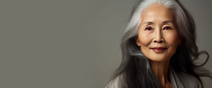 Smiling, elderly, chic Asian woman gray long hair and perfect skin, on creamy beige background, banner. Advertising of cosmetic products, spa treatments, shampoos and hair care products dentistry and medicine perfumes and cosmetology for senior women