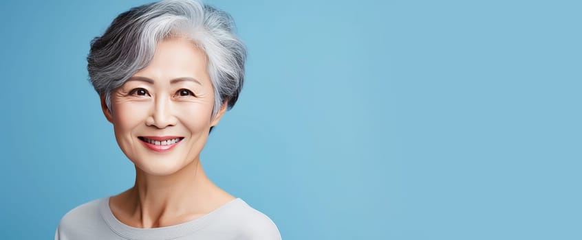 Elegant, smiling, elderly, chic Asian woman with gray hair and perfect skin on light blue background banner. Advertising of cosmetic products, spa treatments, shampoos and hair care products, dentistry and medicine, perfumes and cosmetology for women