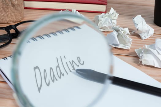 Magnifying glass on notepad with word deadline and trash paper background on office desk. Business concept.
