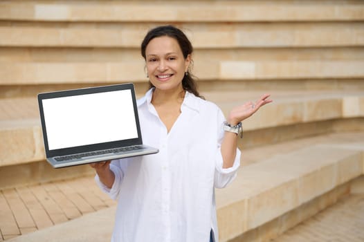 Confident female sales manager, trader, freelance entrepreneur broadly smiling looking at camera, holding laptop with white mockup digital screen. Copy advertising space