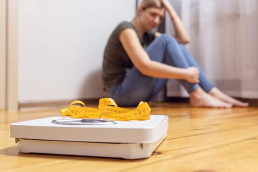 White scale and depression, upset and sad woman with measuring tape on wooden floor.