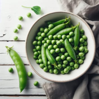 Fresh green peas in bowl with pods and leaves on white wooden table, healthy green vegetable or legume.