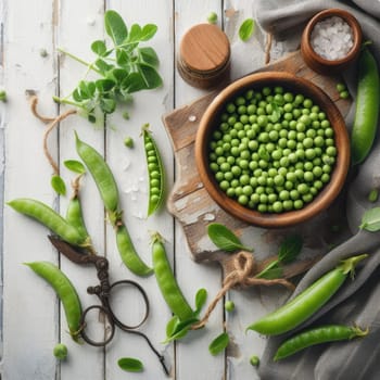 Fresh green peas in bowl with pods and leaves on white wooden table, healthy green vegetable or legume.