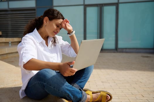 Multitasking businesswoman, manager, entrepreneur online working on laptop, thinking on strategy of business development and sales growth, sitting on steps outdoors. Brainstorming. People. Career