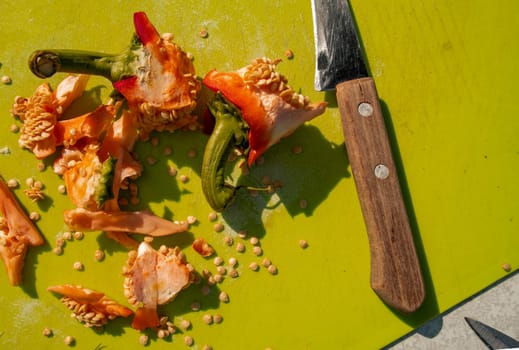 Cooking and cutting sweet peppers, close-up knife, seeds, peel on a green cutting board, top view.