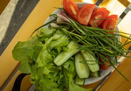 Fresh vegetables - lettuce, green onion, tomatoes and cucumbers on a white plate on a wooden background. The concept of cooking healthy food. View from above.