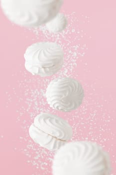 Soaring white zephyr marshmallow on pink background with sugar powder flying food levitation.