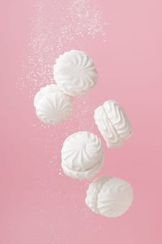 Soaring white zephyr marshmallow on pink background with sugar powder flying food levitation.