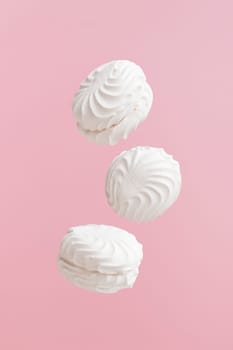 Soaring white zephyr marshmallow on pink background. flying food levitation, sweet candy dessert.