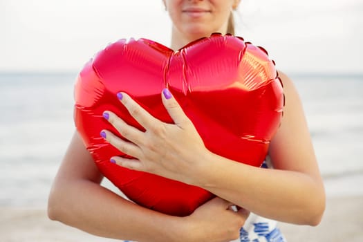 Happy young woman huging heart-shaped balloon on the beach.