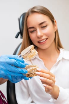 A dentist, gloved and prepared, holds a human jaw model to elucidate a treatment approach to a patient