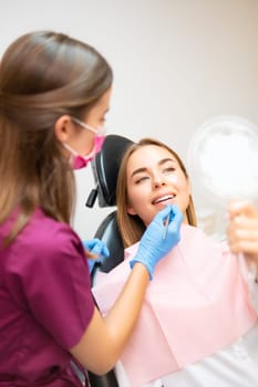The attractive woman checks her beautiful smile in the mirror following her teeth treatment.