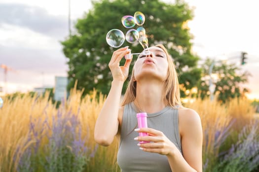 A smiling lady with long hair blows soap bubbles, spreading happiness in the park during the evening.