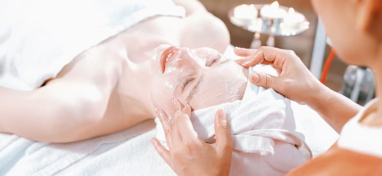 Portrait of beautiful caucasian woman having facial massage with homemade facial mask while lies on spa bed surrounded by beauty electrical equipment and peaceful nature environment. Tranquility.