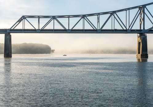 Fisherman in water of Upper Mississippi on calm misty morning by Julien Dubuque Bridge