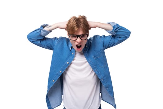 young joyful surprised red-haired guy dressed in a blue shirt wears glasses on a white background with copy space.