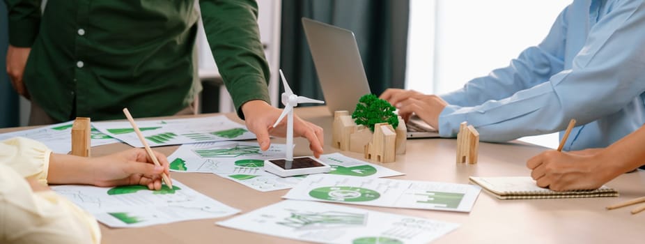 Windmill model represented renewable energy and wooden block represented eco city was placed on green business meeting table with environmental document scatter around. Front view. Delineation.