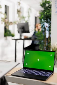 Laptop with chroma key green screen on desk in business office for financial presentation mock up. Portable computer with empty display for financial report in corporate coworking space