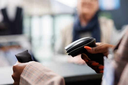 African american worker scanning fashionable shirt using store scanner, preparing purchase for elderly shopaholic woman. Client buying casual wear in clothing store, commercial activity. Close up