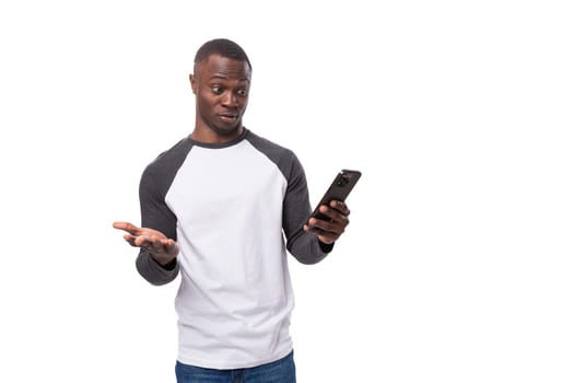 a young American guy with a short haircut dressed in a long-sleeve sweater looks indignantly at a smartphone.