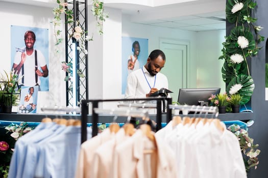 Clothing store african american employee working at counter, planning sales and writing in organiser. Shopping mall fashion department assistant standing at checkout desk