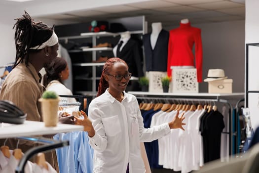 Clothing store owner talking with influencer and showing apparel in stock to create advertisement. Shopping mall worker chatting with fashion blogger and displaying garment for promotion