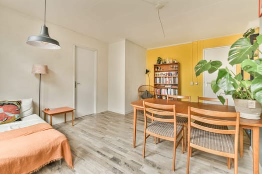 a living room with yellow walls and wood flooring, including a small dining table surrounded by two wooden chairs