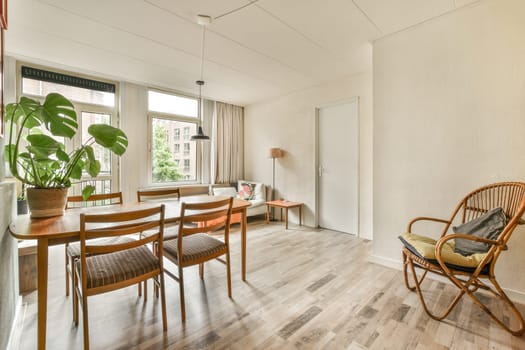 a dining table and chairs in a living room with wood floors, white walls and large windows looking out onto the street