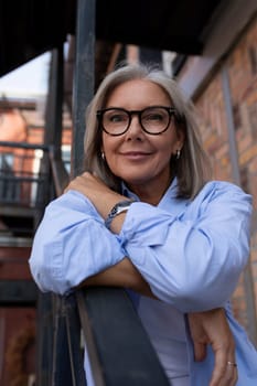 a mature woman with gray hair and glasses walks around the city in summer.