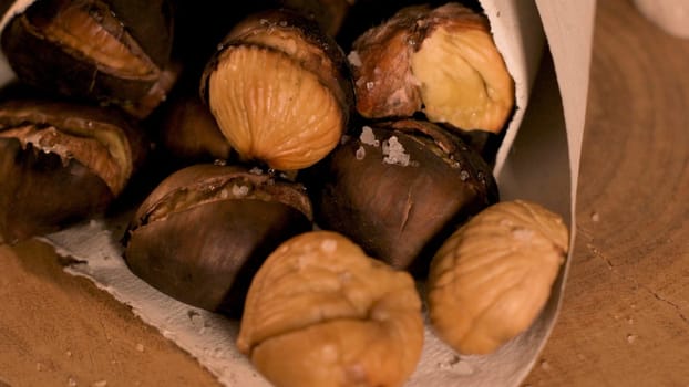 Roasted chestnuts in a paper cone, on a rustic kitchen countertop.