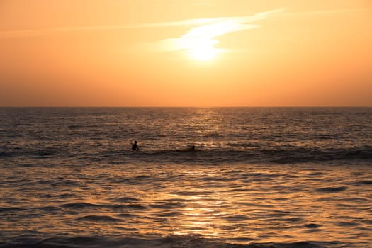 Surfer silhouettes in the Atlantic Ocean from Furadouro Beach at sunset and golden hour, Ovar - Portugal.